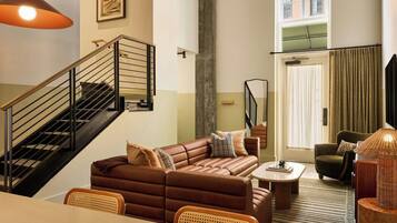 Un salon moderne avec un canapé en cuir marron, une table à manger, des chaises en osier, un escalier avec des rampes noires et une grande fenêtre avec des rideaux.