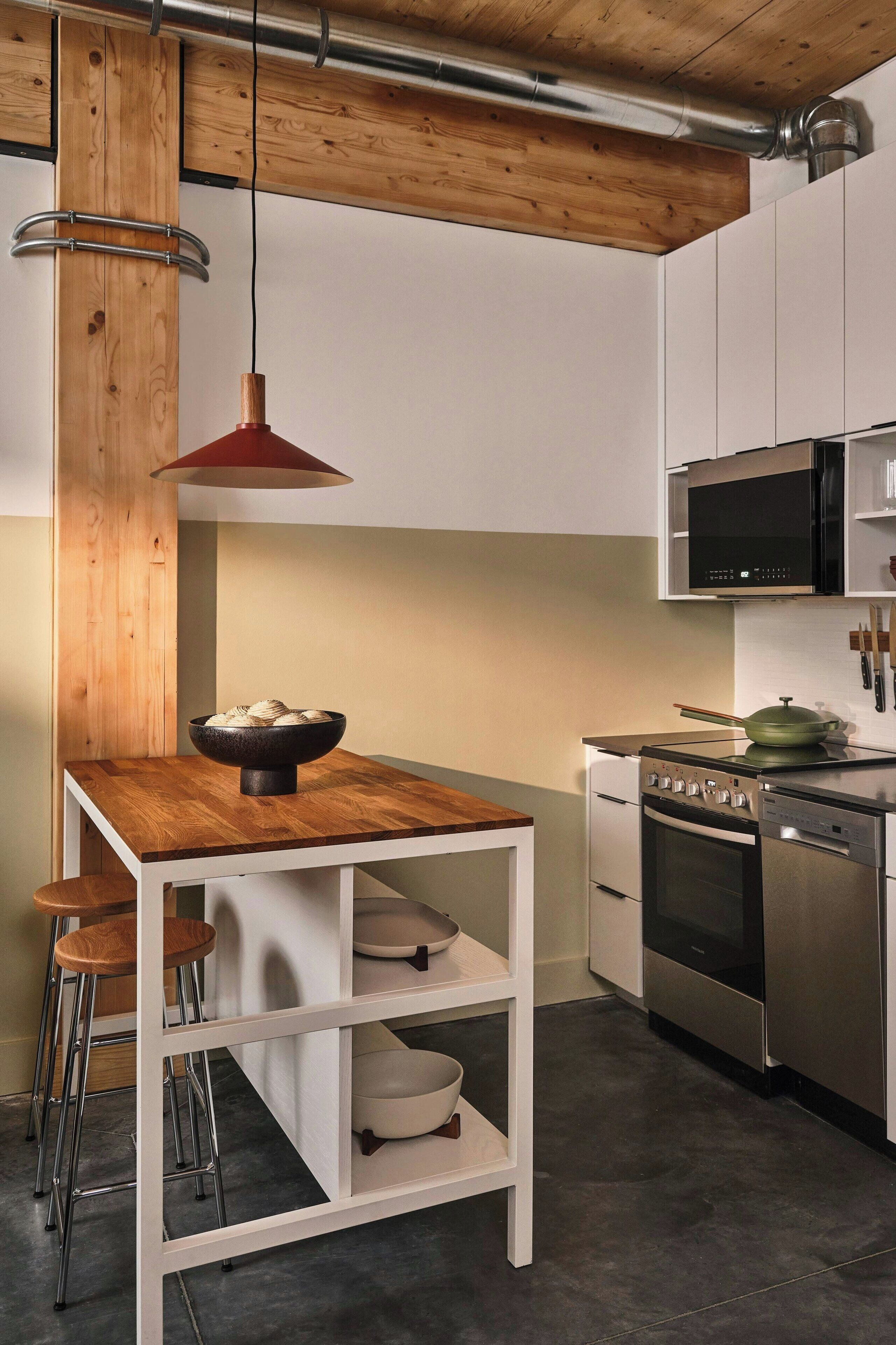 A modern kitchen with a wooden island, bar stools, stainless steel appliances, and a hanging pendant light.