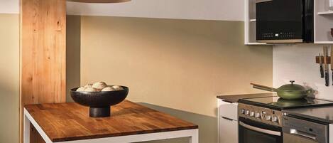 A modern kitchen with a wooden island, bar stools, stainless steel appliances, and a hanging pendant light.