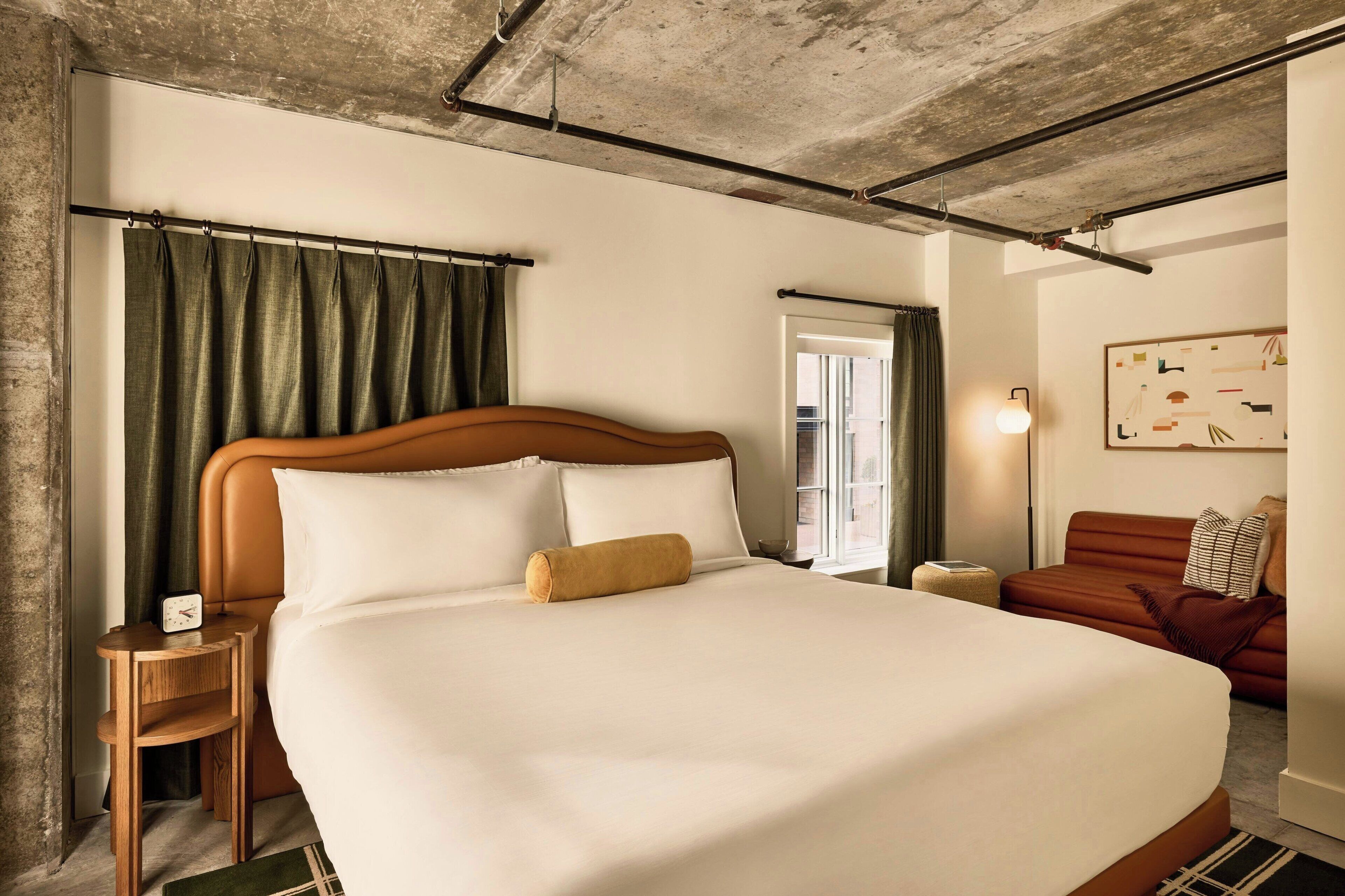 A hotel room with a large bed, a wooden nightstand, a red sofa, and a painting on the wall.