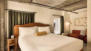 A hotel room with a large bed, a wooden nightstand, a red sofa, and a painting on the wall.