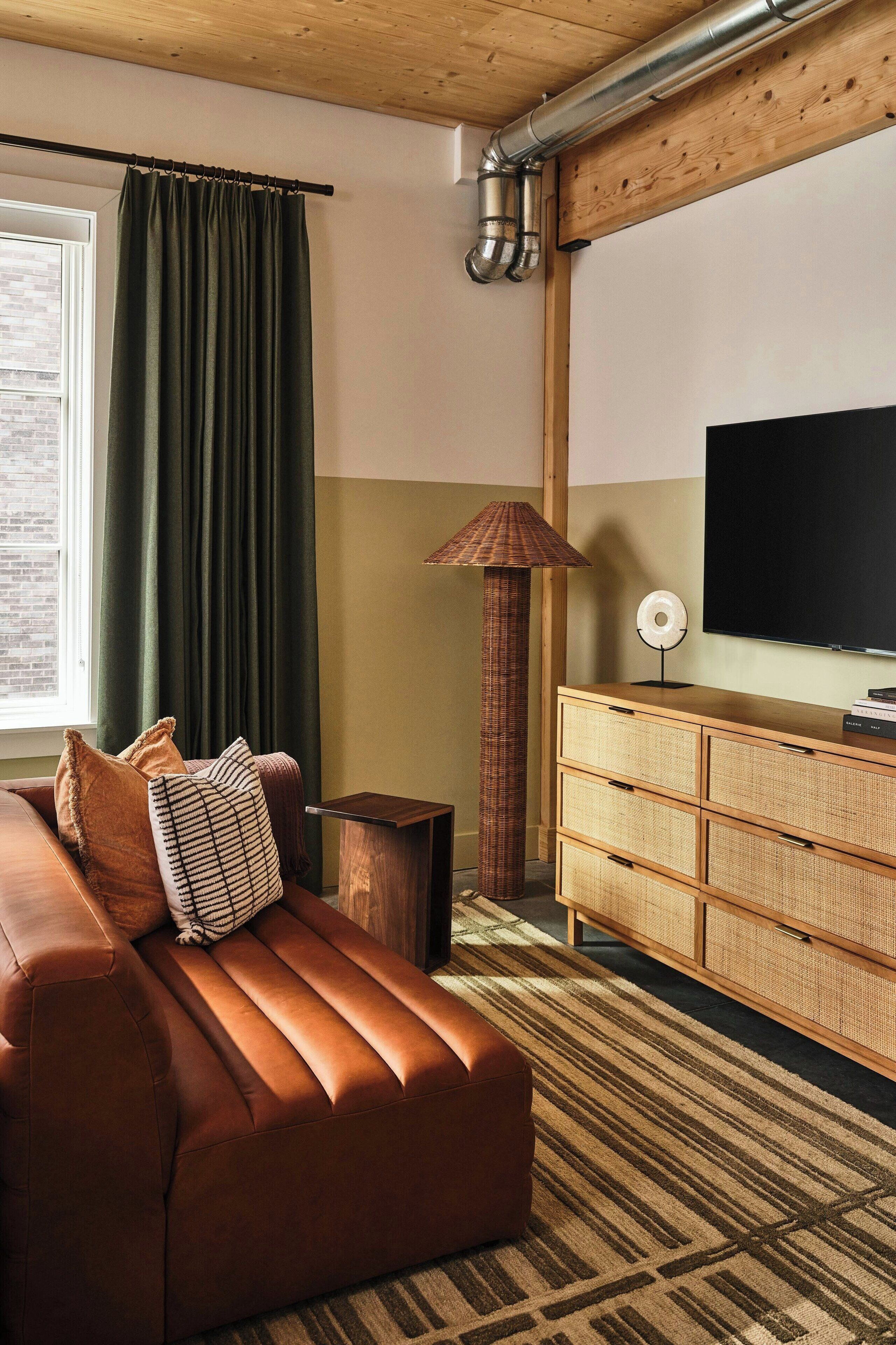 A modern living room with a brown leather sofa, a patterned rug, a wooden cabinet, and a large flat-screen TV.