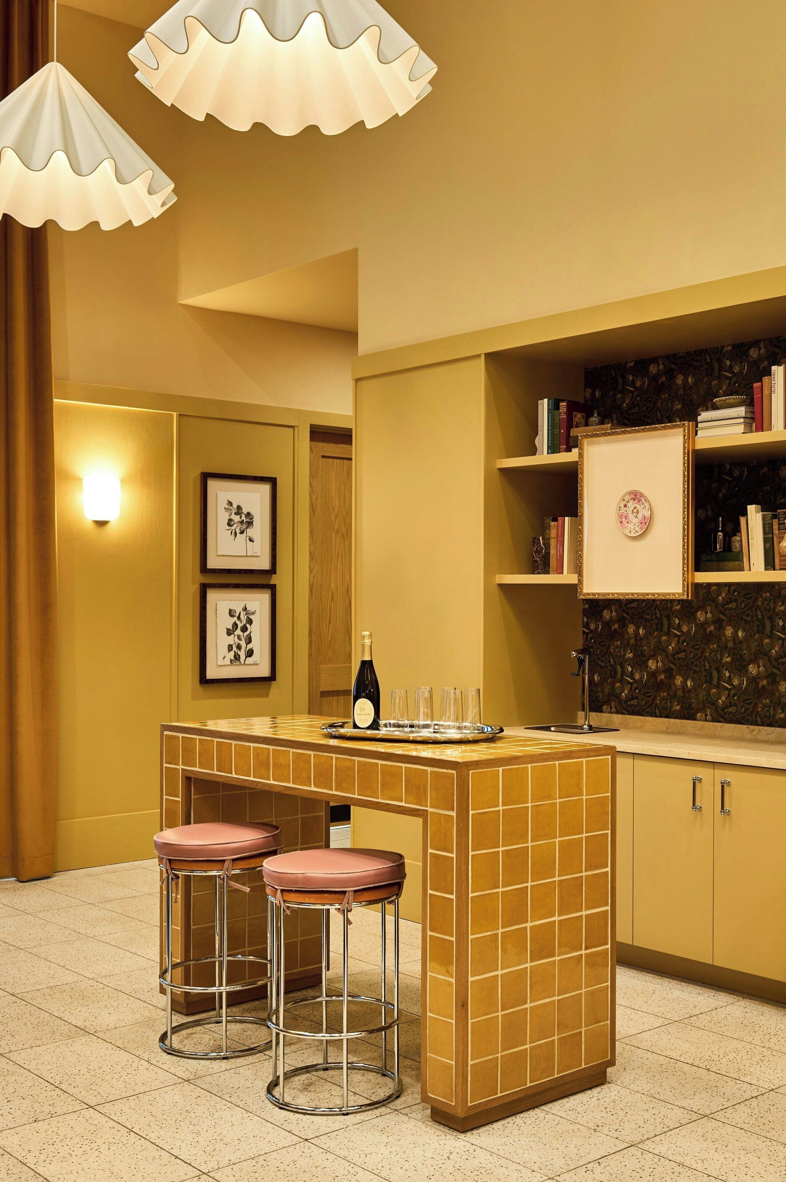 A kitchen with a central island, bar stools, a wine bottle, and framed pictures on the wall.