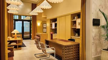 Een hotel receptie met een houten balie, verschillende stoelen, een grote potplant en een bord met de naam van het hotel.