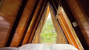 A room with two beds, wooden sloped ceilings, and a view of greenery outside. - Patate Lodge (Patate)