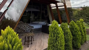 A modern, triangular-shaped building with a glass facade, surrounded by greenery and a wooden deck with outdoor furniture. - Patate Lodge (Patate)