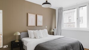 Une chambre à coucher avec un lit, deux tables de chevet, un luminaire suspendu et une fenêtre avec des rideaux.