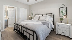 A bedroom with a bed, bedside tables, a ceiling fan, and a door leading to another room.