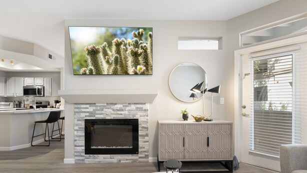 A modern living room with a fireplace, a kitchen in the background, and a large cactus wall art piece.