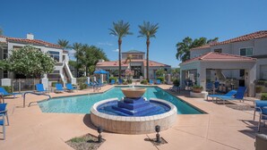 A swimming pool with a central fountain, surrounded by lounge chairs and palm trees.