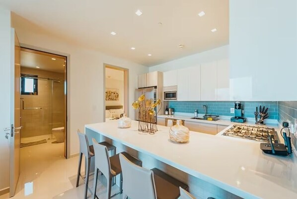 A modern kitchen with a central island, bar stools, and a glass-enclosed shower area.