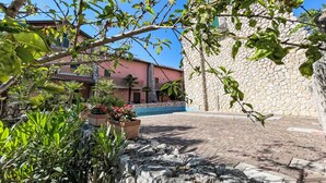 A courtyard with a stone wall, a pool, and a building with a pink facade. - Ville Rio by Interhome (Lignano Sabbiadoro)
