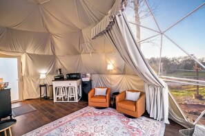 Relax in a cozy tent with a comfortable seating area, kitchenette, and dining table, offering a view of the outdoors.