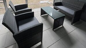 Ein überdachter Patio-Bereich mit Korbmöbeln, darunter eine Couch, Stühle und ein Couchtisch.
