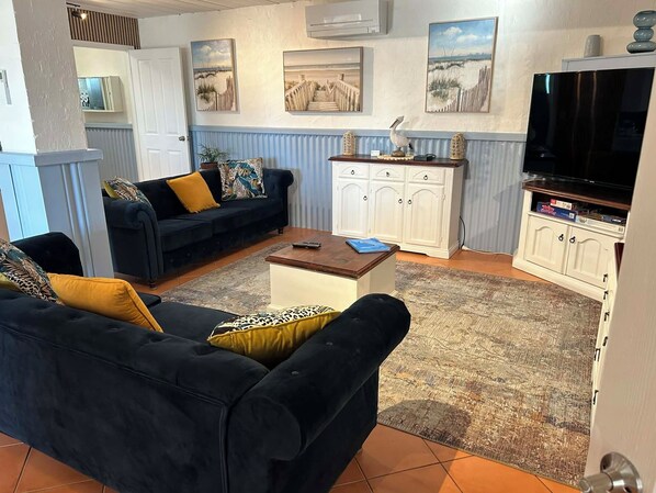 A living room with a black sofa, a coffee table, and a TV. There are paintings on the wall and a cabinet with a TV on top. - Beachfront apartment with pool, 4 minutes walk to Indian Ocean. Sleeps 6 (Quinns Rocks)