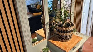 A room with a wooden door, a mirror, a small table with woven baskets, and a view of a living area with a sofa and cushions. - Beachfront apartment with pool, 4 minutes walk to Indian Ocean. Sleeps 6 (Quinns Rocks)