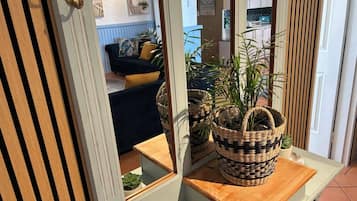 A room with a wooden door, a mirror, a small table with woven baskets, and a view of a living area with a sofa and cushions.