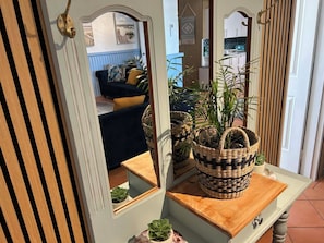 A room with a wooden door, a mirror, a small table with woven baskets, and a view of a living area with a sofa and cushions.