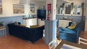 A living room with two blue sofas, a television, and a kitchen area with cabinets and a fire extinguisher. - Beachfront apartment with pool, 4 minutes walk to Indian Ocean. Sleeps 6 (Quinns Rocks)