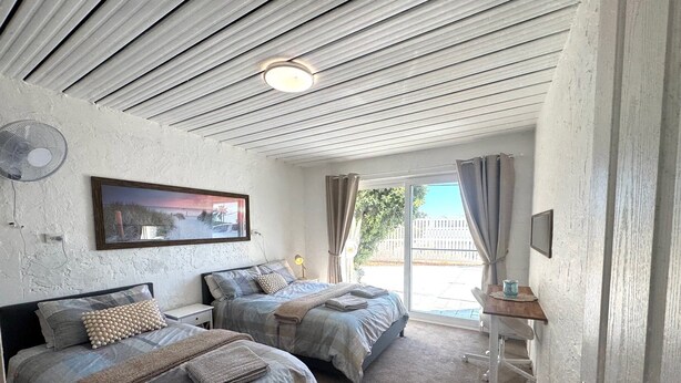 A room with two beds, a ceiling fan, a table with a lamp, and a view of the outdoors through a sliding door. - Beachfront apartment with pool, 4 minutes walk to Indian Ocean. Sleeps 6 (Quinns Rocks)