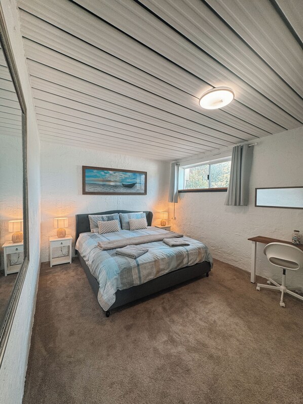 Une chambre à coucher avec un lit, des lampes de chevet, une fenêtre, un bureau et un tableau accroché au mur.