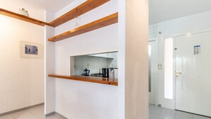 A hallway with a kitchen area visible through a window, wooden beams on the ceiling, and a white door at the end.