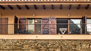 A building with a stone facade, a balcony with metal railings, and a tiled roof.