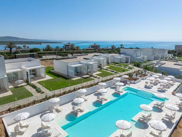 A modern resort with a large pool, outdoor seating, and a view of the sea.