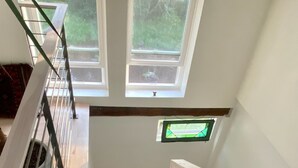 A wooden staircase with a metal railing, a small window with a green frame, and a view of greenery outside.