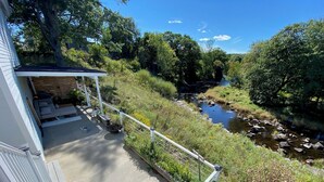 A balcony with a view of a river, surrounded by greenery and a white railing.