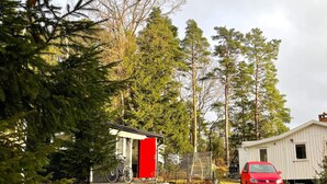 Une cabane avec une porte rouge, un vélo et une voiture rouge garée devant.