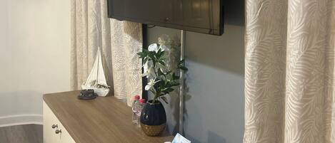 Ein modernes Wohnzimmer mit einem flachbildfernseher an der Wand, einem Holztischchen mit Dekoration und gemusterten Vorhängen.