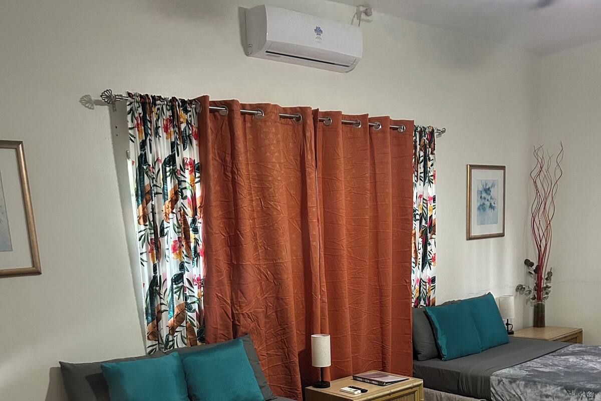 A hotel room with two beds, a checkered floor, a wall-mounted air conditioner, and a framed picture.