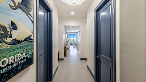 Un corridoio con porte scure, un pavimento in legno chiaro e un lampadario a soffitto.