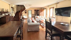 Ein geräumiger Wohnbereich mit einem Holzessttisch, zwei Sofas, einem Fernseher und einer Treppe, die zu einer weiteren Ebene führt.
