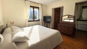 Ein Schlafzimmer mit einem großen Bett, einem Schminktisch, einem Fernseher und einem Fenster mit Vorhängen.