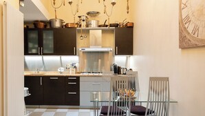 A modern kitchen with a chandelier, checkered floor tiles, and a dining area with metal chairs.