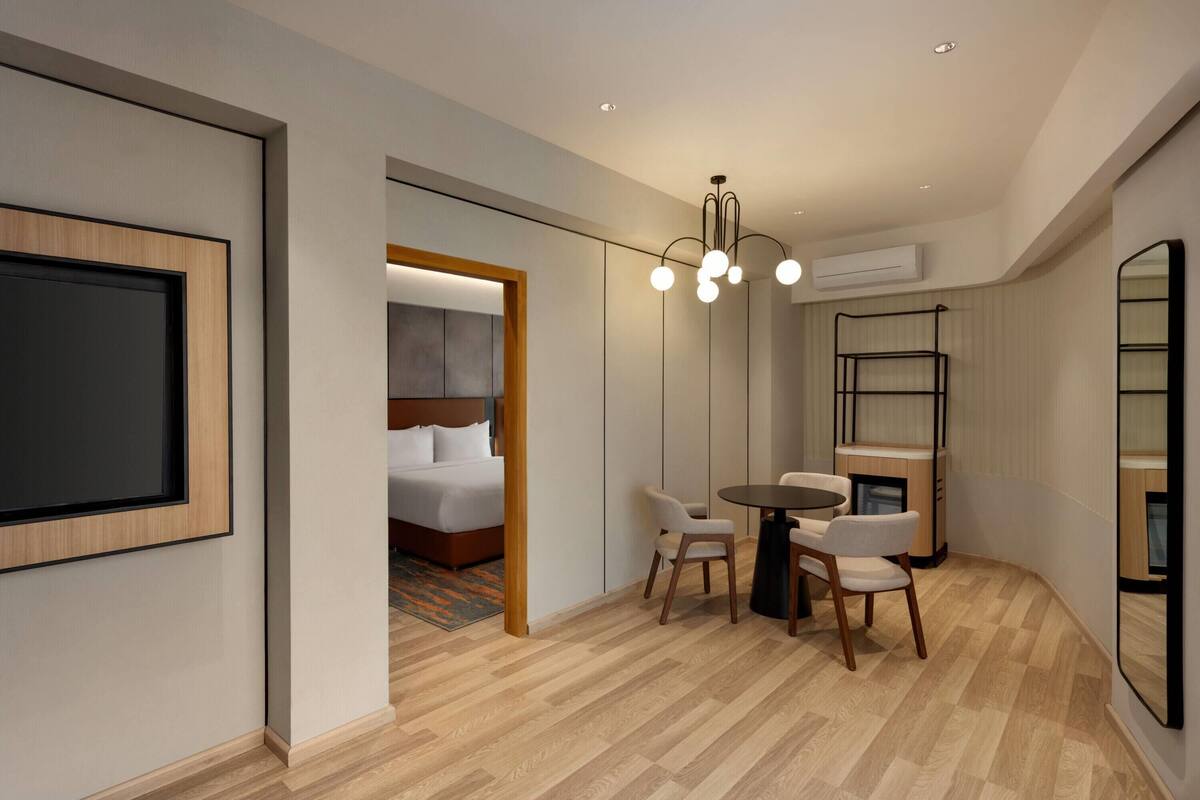 Una habitación de hotel con cama, escritorio y sillas, lámpara colgante y un espejo grande.