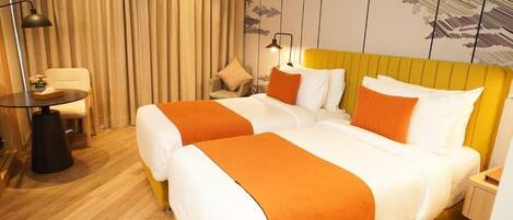 A hotel room with two beds, a desk, a chair, and a large window with curtains.