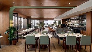 A modern restaurant with wooden ceiling and walls, green upholstered chairs, and a bar area with shelves of bottles. - Ramada Encore by Wyndham Gurugram Dwarka Expressway (Gurugram)