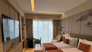 A hotel room with two beds, a desk, a chair, a TV, and a large window with curtains. - Ramada Encore by Wyndham Gurugram Dwarka Expressway (Gurugram)