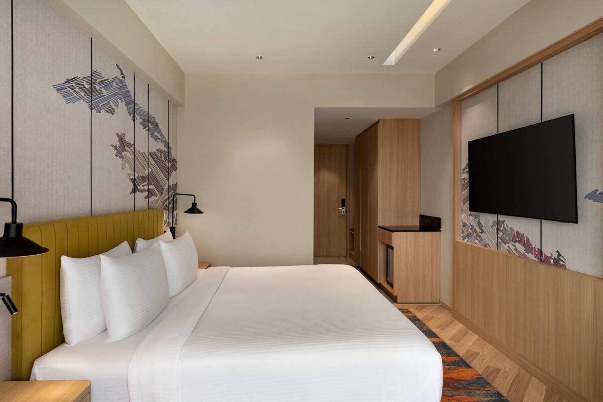 Habitación de hotel con una cama grande, un televisor de pantalla plana montado en la pared, un armario de madera y un panel decorativo.