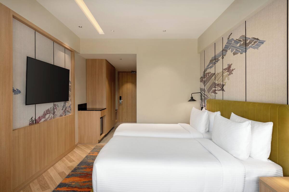 Habitación de hotel con dos camas, un televisor de pantalla plana, paneles de madera, una obra de arte grande en la pared y suelo alfombrado.