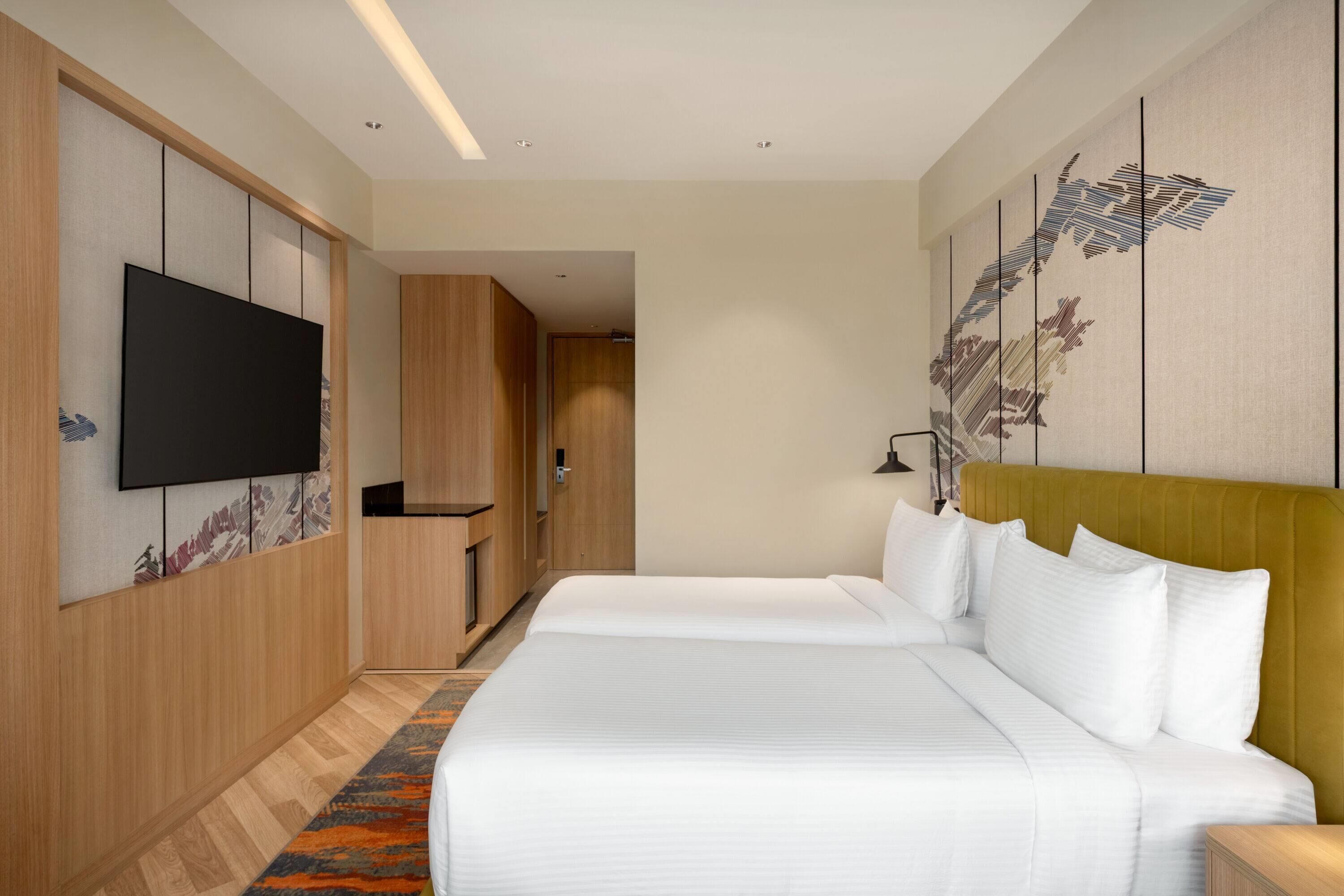A hotel room with two beds, a flat-screen TV, wooden paneling, and a large artwork on the wall.