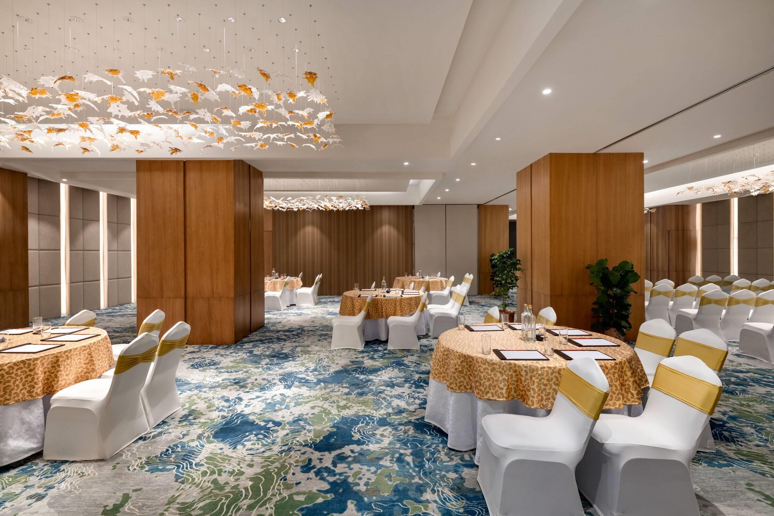 Une salle de banquet avec des tables rondes, des chaises blanches et un tapis à motifs.
