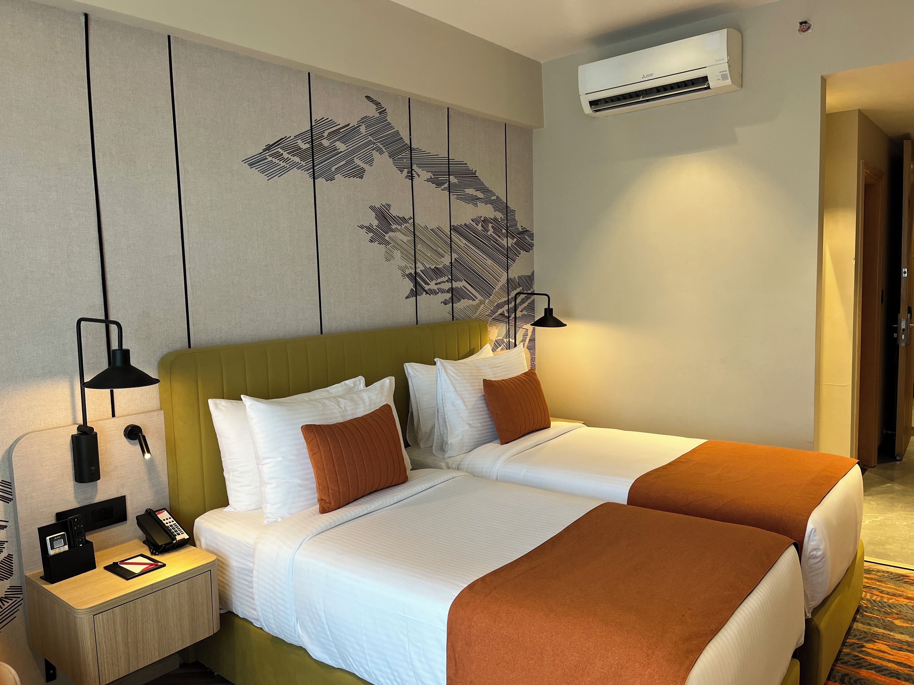 Habitación de hotel con dos camas, una mesita de noche con lámpara, teléfono y aire acondicionado instalado en la pared.