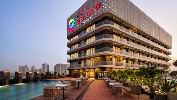 A multi-story hotel with a rooftop pool area, outdoor seating, and a view of the city skyline. - Ramada Encore by Wyndham Gurugram Dwarka Expressway (Gurugram)