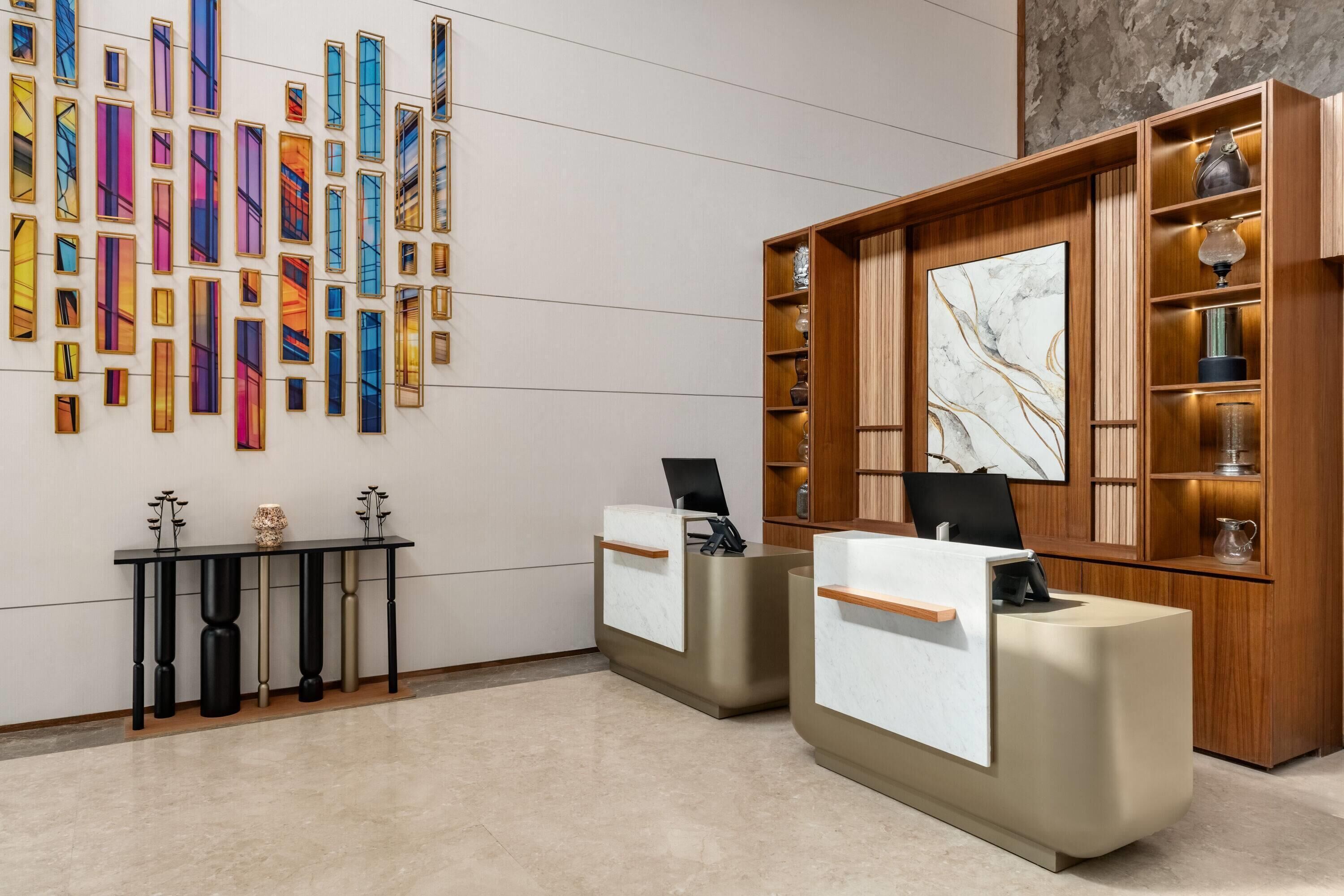 A reception area with two reception desks, a wall with colorful vertical panels, and a wooden shelving unit with decorative items.