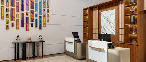 A reception area with two reception desks, a wall with colorful vertical panels, and a wooden shelving unit with decorative items.