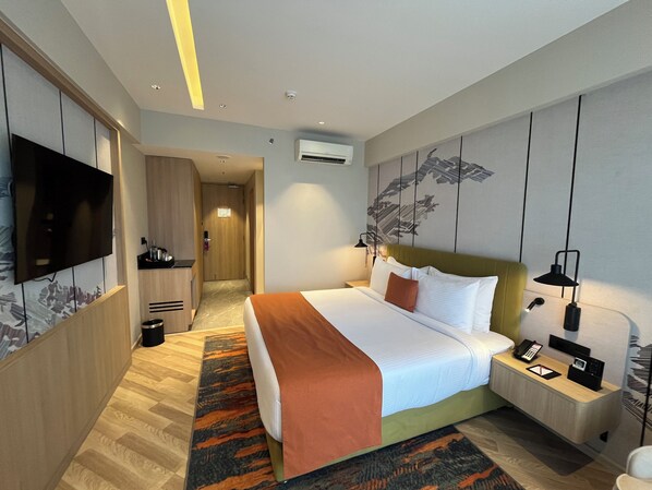 Habitación de hotel con cama, mesita de noche, lámpara y televisor de pantalla plana en la pared.